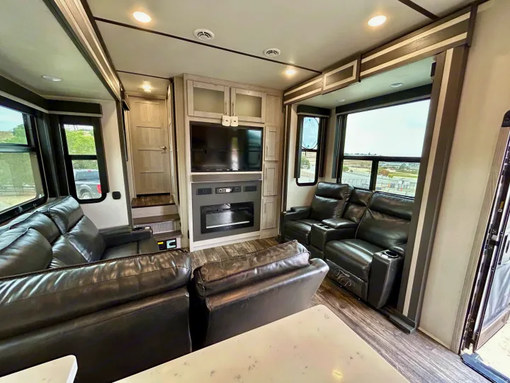 Modern RV rental interior: cozy living room with black leather recliners, entertainment center, and fireplace.. Keystone Fuzion 2022