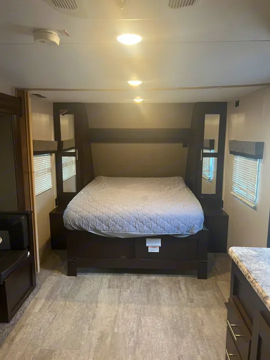Spacious RV rental bedroom with a comfortable queen bed, sleek dark wood furniture, and bright overhead lighting.. K-Z Manufacturing Sportsmen 2019