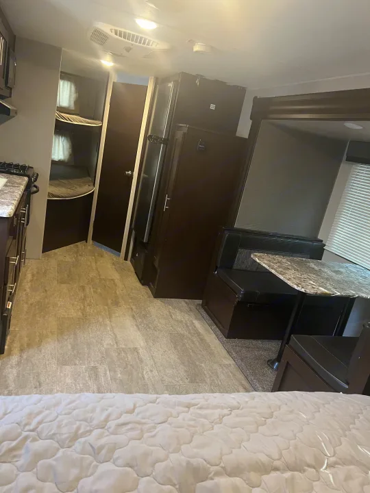 Spacious RV rental interior with light flooring and dark wood furniture, featuring a kitchen, dining area, and bunk beds.. K-Z Manufacturing Sportsmen 2019