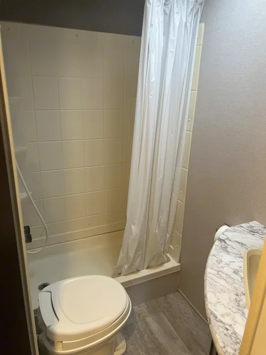 This RV rental bathroom features a white toilet, tiled shower with curtain, and a marble-patterned sink vanity.. K-Z Manufacturing Sportsmen 2019