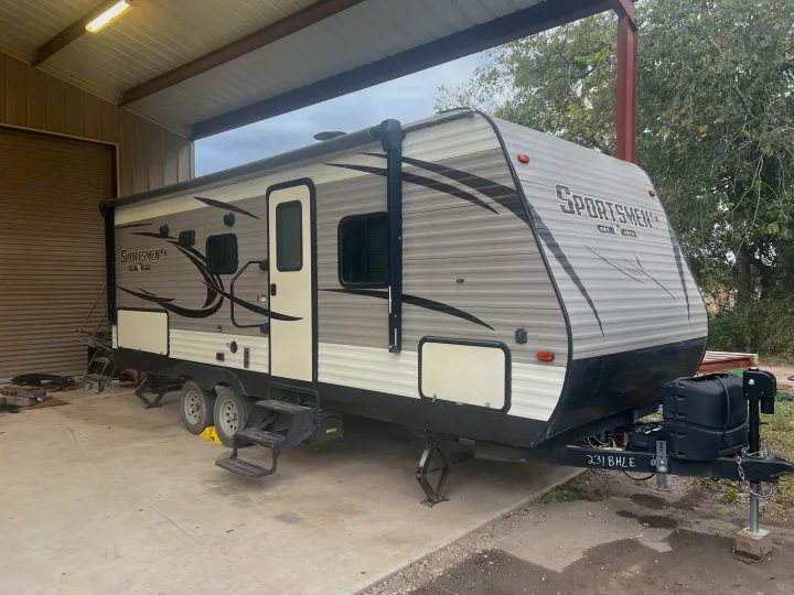 Grey "Sportsmen" travel trailer, perfect for your next RV rental adventure. Parked under a shed with steps down.. K-Z Manufacturing Sportsmen 2019
