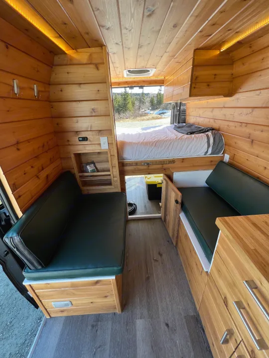 Inviting wooden RV rental interior with bed, built-in seating, and storage. Ideal for adventurers.. Dodge Van 2024