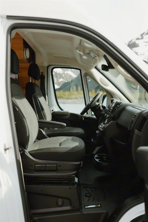 RV rental camper van interior. Front seats and dashboard visible, offering a stunning view of mountains and a lake.. Dodge Van 2024