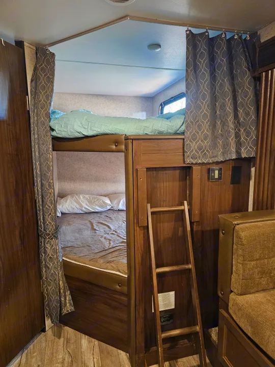 RV rental interior features bunk beds with privacy curtains, a ladder, and integrated controls, maximizing sleeping space.. Forest River Cherokee Grey Wolf 2019