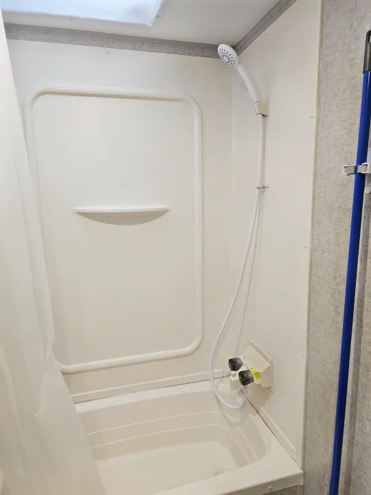 Inside an RV rental: a compact, clean white shower/bathtub unit with a handheld showerhead, water controls, and a small shelf.. Forest River Cherokee Grey Wolf 2019
