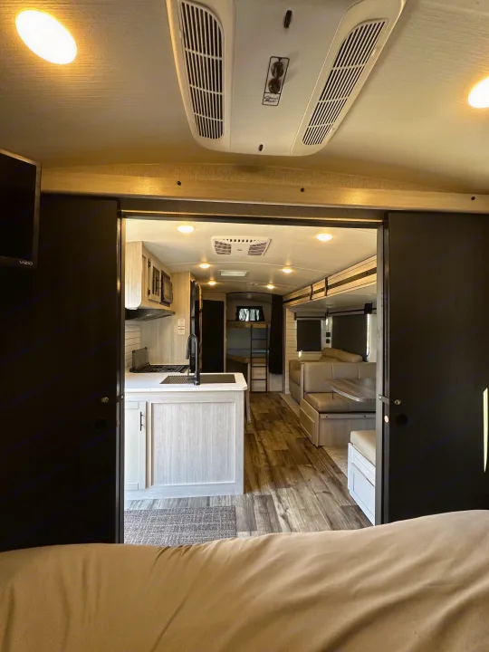 Spacious RV rental interior. View from the bedroom into a modern kitchen, dining booth, and bunk bed area.. Keystone RV Sunset Trail 2024