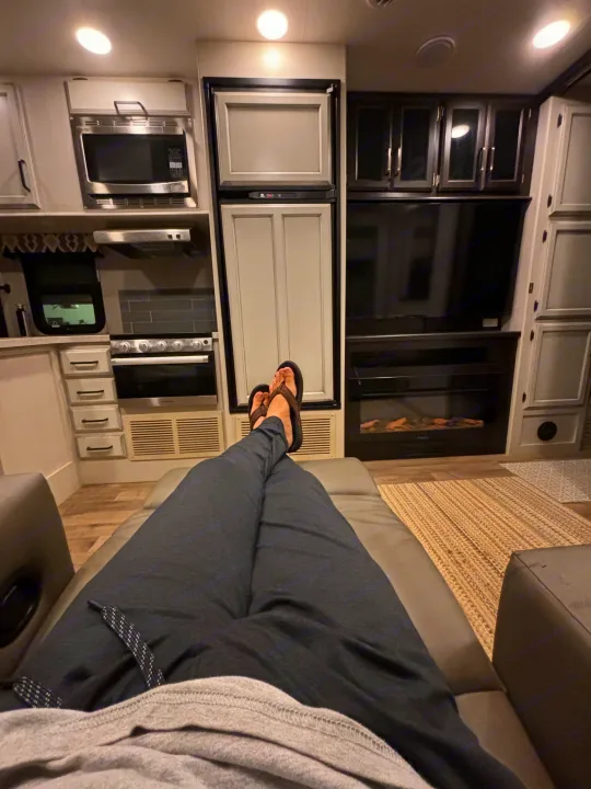 An RV rental offers comfort: modern kitchen, fridge, TV, fireplace visible, with a person relaxing.. Entegra Coach Odyssey 2021