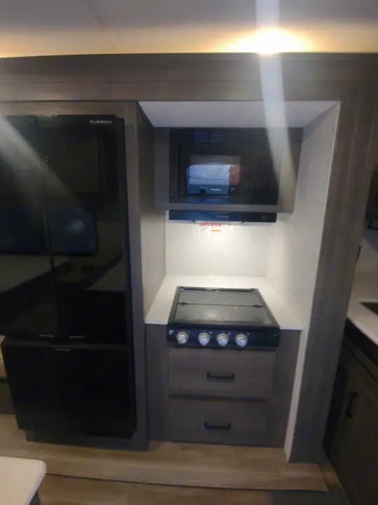 Modern RV rental kitchen appliances: a Furrion refrigerator, microwave, and stove with cabinet storage.. Grand Design Transcend 2025