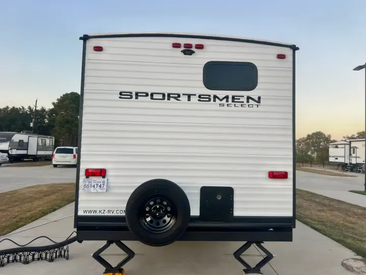 Rear view of a white Sportsmen Select RV, ready for an rv rental. Shows spare tire, license plate, and leveling jacks.. Other Other 2024