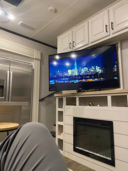 Relax in your RV rental! Enjoy a cityscape on TV, with a cozy fireplace below and a modern fridge nearby.. Highland Ridge RV Open Range 2024