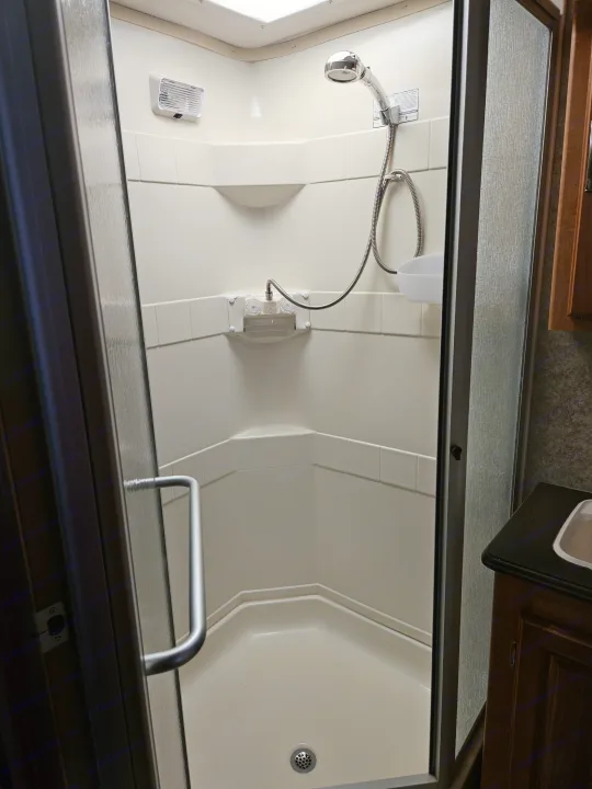 Inside a compact RV rental shower: frosted door, corner shelves, vent/light, and handheld shower. Efficient design.. Coachmen Mirada 2007