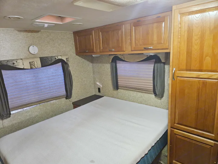 This inviting RV rental bedroom features a comfortable bed, wooden storage cabinets, two windows with blinds, and safety features.. Coachmen Mirada 2007