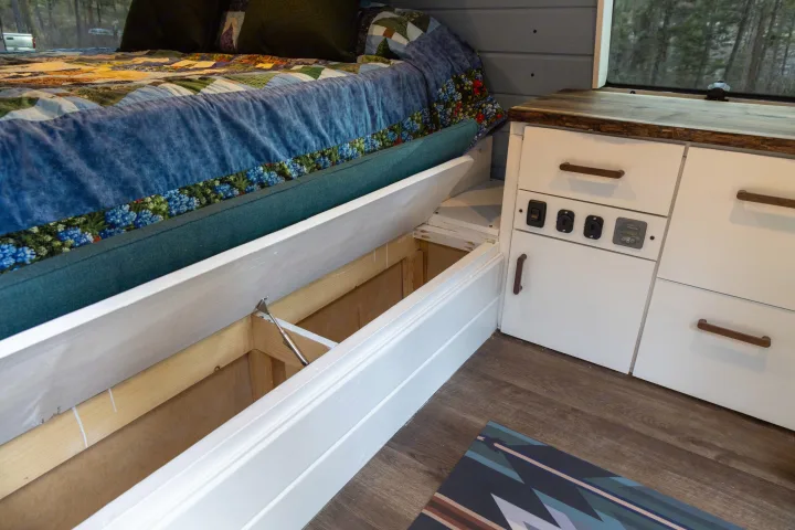 Clever storage in this cozy RV rental! An under-bed compartment is open, beside white cabinets with controls.. Ford Econoline 150 2009