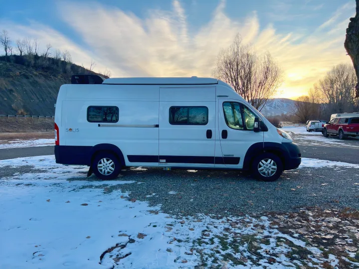 White Winnebago Solis camper van for RV rental, parked in a snowy setting with a sunset over mountains.. Winnebago Winnebago 2023