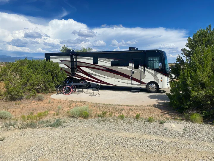 A large Encore RV rental is set up at a desert campsite, featuring bikes, patio furniture, and scenic mountain views.. Coachmen Encore 2022