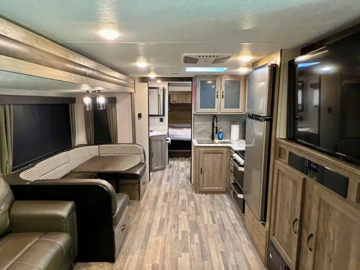 A bright rv rental interior showcasing a full kitchen, dining booth, sofa, entertainment, and bedroom access.. Forest River Vibe 2020