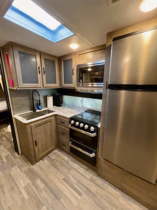Modern RV rental kitchen features stainless steel appliances, a spacious sink, and stylish light wood cabinets.. Forest River Vibe 2020