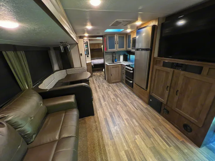 This bright rv rental interior features a living area with a sofa and dinette, a full kitchen, and a bedroom visible beyond.. Forest River Vibe 2020