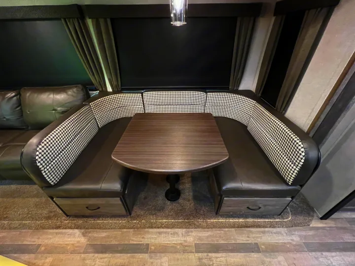 Spacious RV rental dinette with houndstooth and faux leather seating, dark table, and window shades. Features storage.. Forest River Vibe 2020