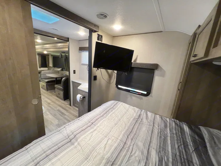 RV rental interior: bedroom with TV, looking towards a dining booth & small sink. Features a skylight & cozy living space.. Forest River Vibe 2020