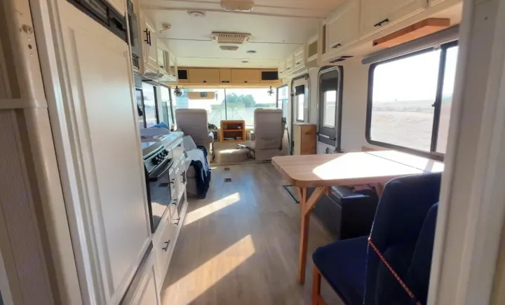 Interior of a bright RV rental showing the kitchen, dining table, and front driving area, ideal for mobile living.. Four Winds Windsport 2001