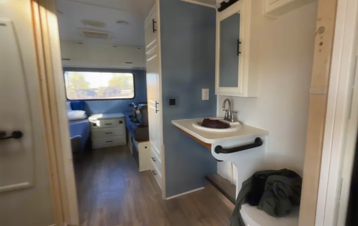 RV rental interior: A compact sink vanity on the right, facing a cozy bed and white storage cabinets on the left.. Four Winds Windsport 2001