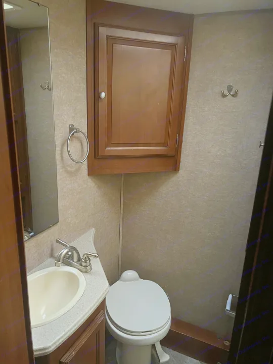 A compact RV rental bathroom featuring a sink, toilet, mirror, and a wooden wall cabinet. Functional and efficient.. Coachmen Leprechaun 2015