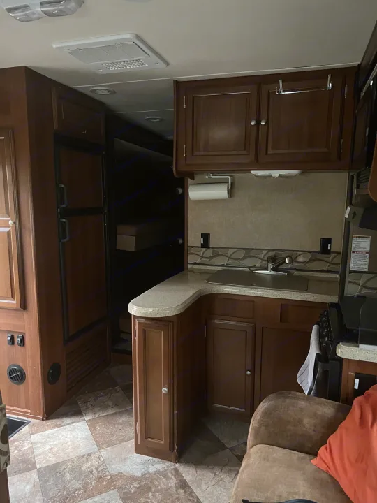 RV rental interior showing a kitchen, refrigerator, and sleeping bunks. Ideal for travel and comfortable living.. Coachmen Leprechaun 2015