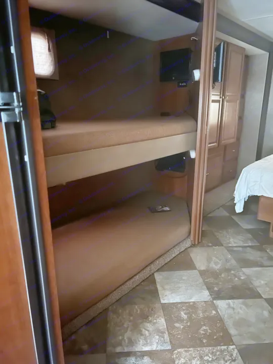 An RV rental interior features two built-in bunk beds with TVs, wood cabinets, and a partial view of another bed.. Coachmen Leprechaun 2015