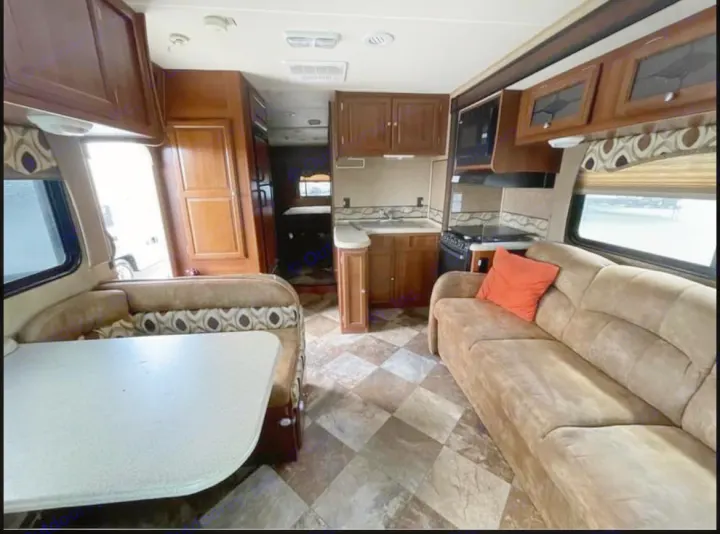 Spacious RV rental interior with kitchen, dinette, and sofa. Features warm wood cabinets, checkered floor, and comfy seating.. Coachmen Leprechaun 2015