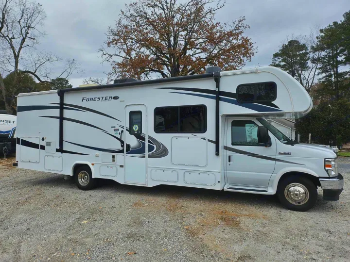A white Class C rv rental with black and grey graphics is parked on a gravel surface, ready for travel adventures.. Forest River Forester 2021