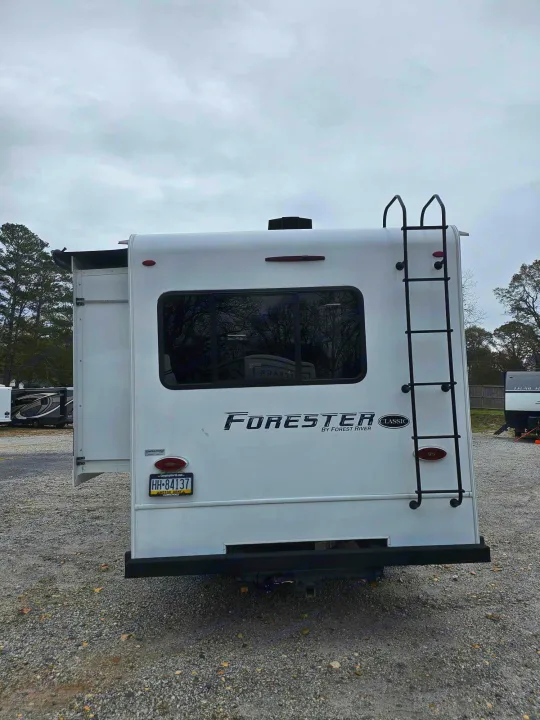 White Forester motorhome, ideal for RV rental. Rear view shows a ladder, window, and an extended slide-out ready for camping.. Forest River Forester 2021