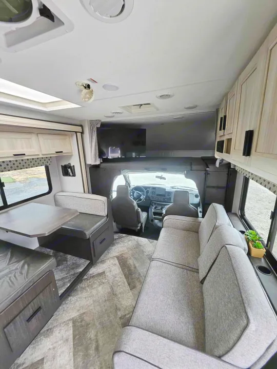 Explore this clean RV rental interior with a cozy sofa, dining area, overhead bunk, and front cockpit. Ideal for road trips.. Forest River Forester 2021