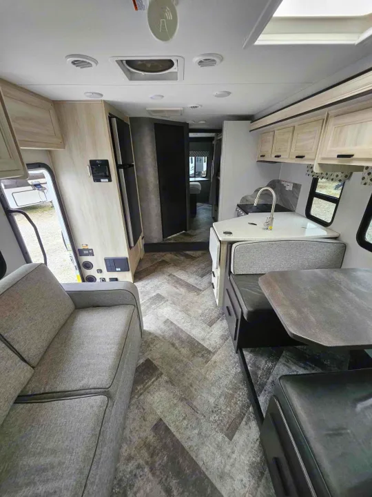 Modern RV rental interior with grey sofa, kitchenette, and dinette. Light-wood cabinets, herringbone floor. Ready for travel comfort.. Forest River Forester 2021