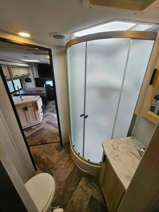 Discover this modern RV rental's interior: a compact bathroom with a curved shower, toilet, and vanity, reflecting the living space.. Forest River Forester 2021