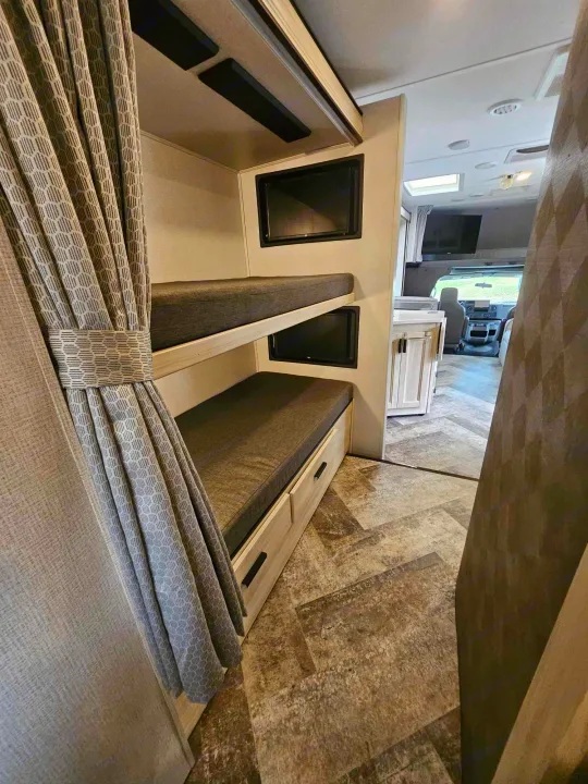 Inside an rv rental, showing a cozy bunk bed area with integrated TVs. The modern interior leads to the driver's cab.. Forest River Forester 2021