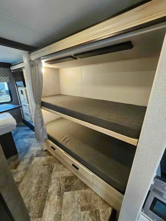 Inside this RV rental, find comfortable bunk beds with dark mattresses and a privacy curtain, perfect for extra sleeping space.. Forest River Forester 2021