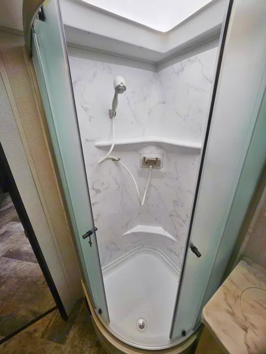 Bright RV rental shower with white marble-look walls, a skylight overhead, and a convenient handheld showerhead.. Forest River Forester 2021