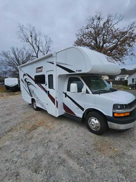 White Coleman Thor RV rental parked on gravel, with an Outback travel trailer in the background under an overcast sky.. Thor Motor Coach Other 2024