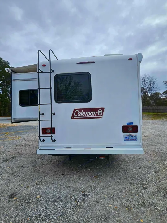 Rear view of a white Coleman RV rental. Features a ladder, NC license plate KMW-6169, and extended side slide-out, parked on gravel.. Thor Motor Coach Other 2024
