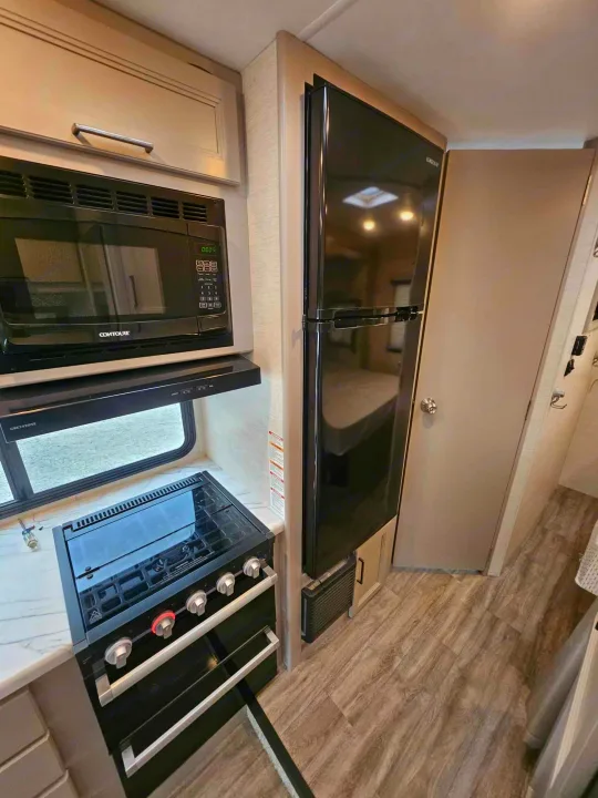 RV rental kitchen showcasing black microwave, gas stove/oven, and large refrigerator. A functional and modern RV interior space.. Thor Motor Coach Other 2024