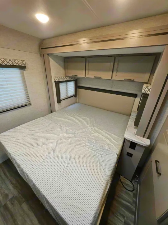 Bright RV rental bedroom featuring a large bed, overhead storage, and windows with blinds.. Thor Motor Coach Other 2024