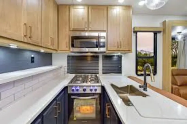 Cozy, modern RV rental kitchen: light wood cabinets, white counters, stainless appliances, and a window view.. Heartland Cyclone 2025