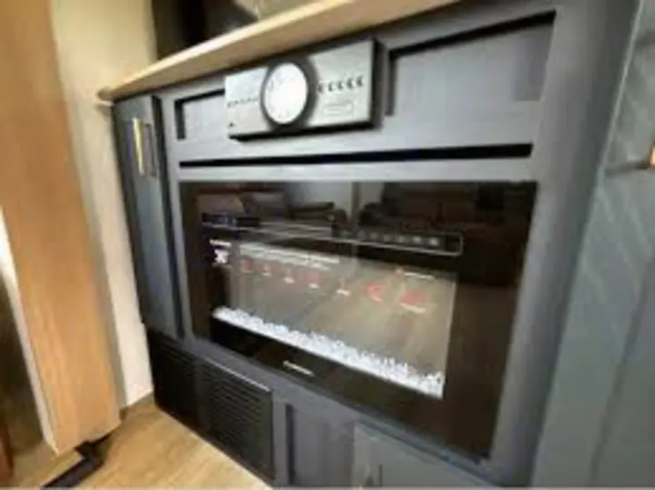 Inside an RV rental: a built-in electric fireplace with digital controls, part of a cozy entertainment setup, for comfortable travel.. Heartland Cyclone 2025
