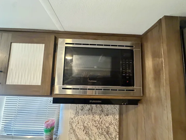 Furrion stainless steel microwave and hood in a modern RV rental kitchen, integrated into wood cabinetry.. Avenger Avenger Trailer 2022
