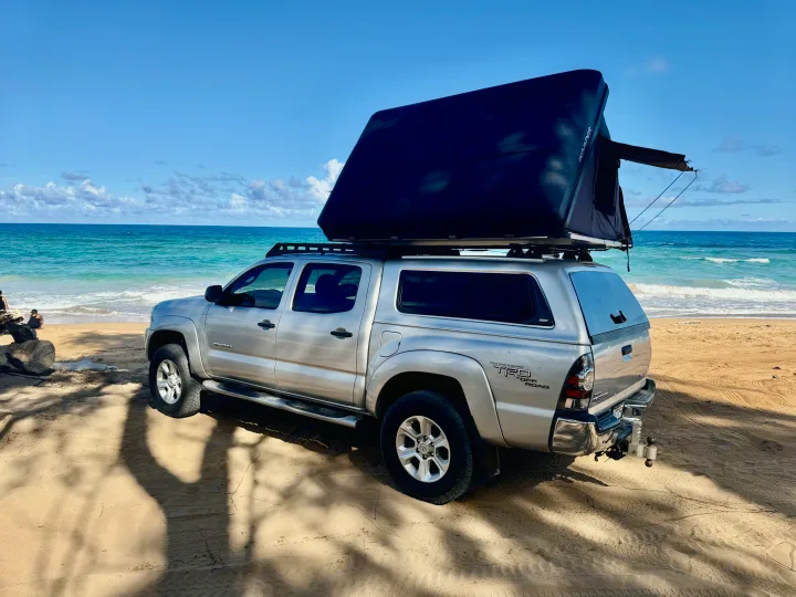 A silver Toyota Tacoma truck with an iKamper rooftop tent on a sandy beach, perfect for your next RV rental adventure.. Toyota Tacoma 2010