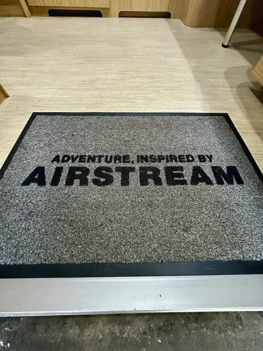Doormat with 'ADVENTURE. INSPIRED BY AIRSTREAM' inside an RV rental, showing light wood floor and cabinetry.. Airstream Flying Cloud 2019