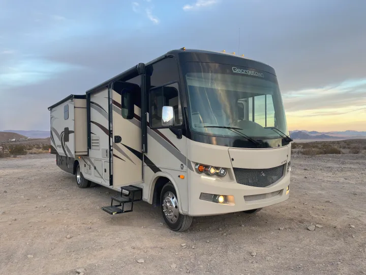 A large Georgetown rv rental motorhome with extended side and steps down, parked on a dirt road in a vast desert at dusk.. Forest River Georgetown 2019