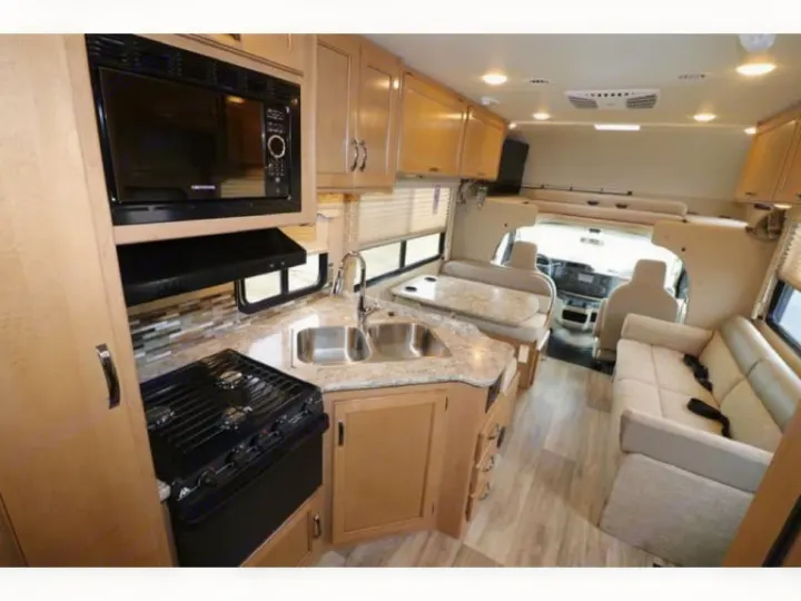 A well-equipped rv rental interior showing a kitchen with microwave/stove/sink, dining booth, and living room sofa.. Thor Freedom Elite 2017
