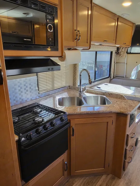 RV rental kitchen features microwave, stove, sink, and ample cabinets for a comfortable cooking experience.. Thor Freedom Elite 2017